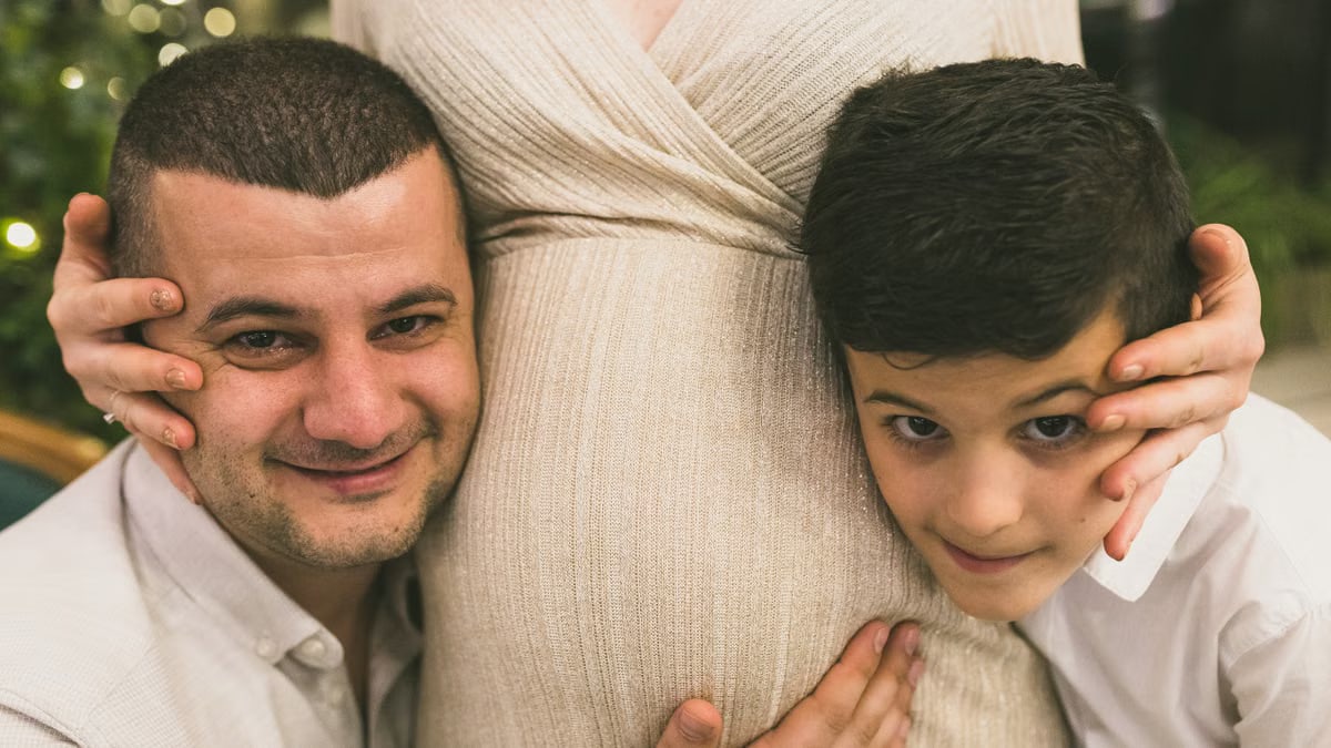 A joyful family moment with father and son embracing the pregnant mother, symbolizing love and togetherness.