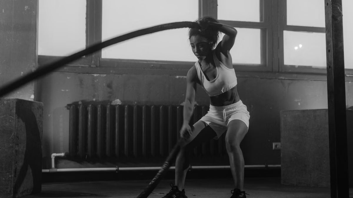 Woman in a gym engaging in vigorous battle rope workout for fitness.